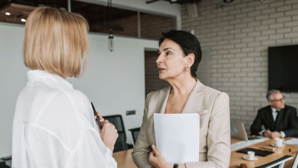Two women engage in a conversation during a professional meeting in a modern office