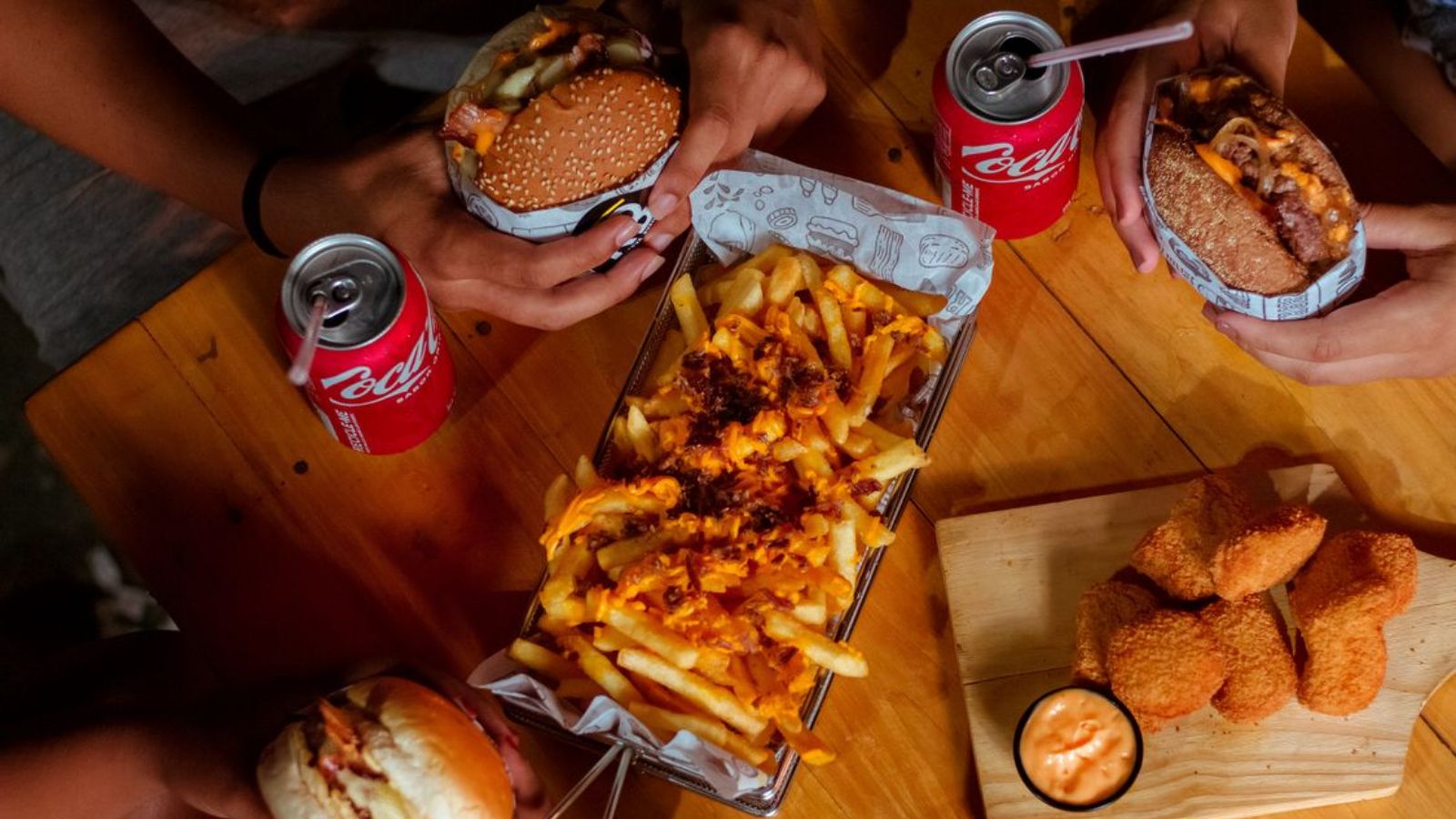 Hed Been Covering Meals for His Girlfriend and Her Sisters for a While — He Finally Said He Couldnt Afford It Anymore Fast food meals for sharing, including burgers, fries, nuggets, and drinks on a wooden table