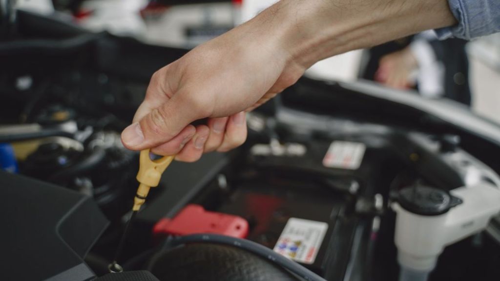 Hand checking oil dipstick in a car engine bay for maintenance and diagnostics