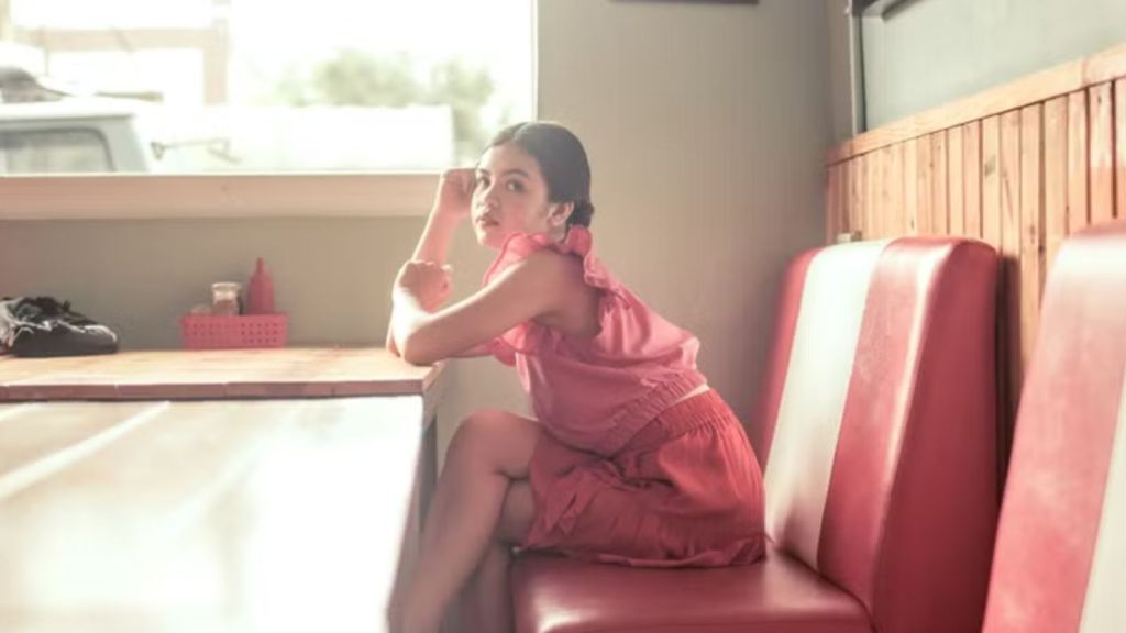 Young woman in pink dress sitting and relaxing at a retro diner