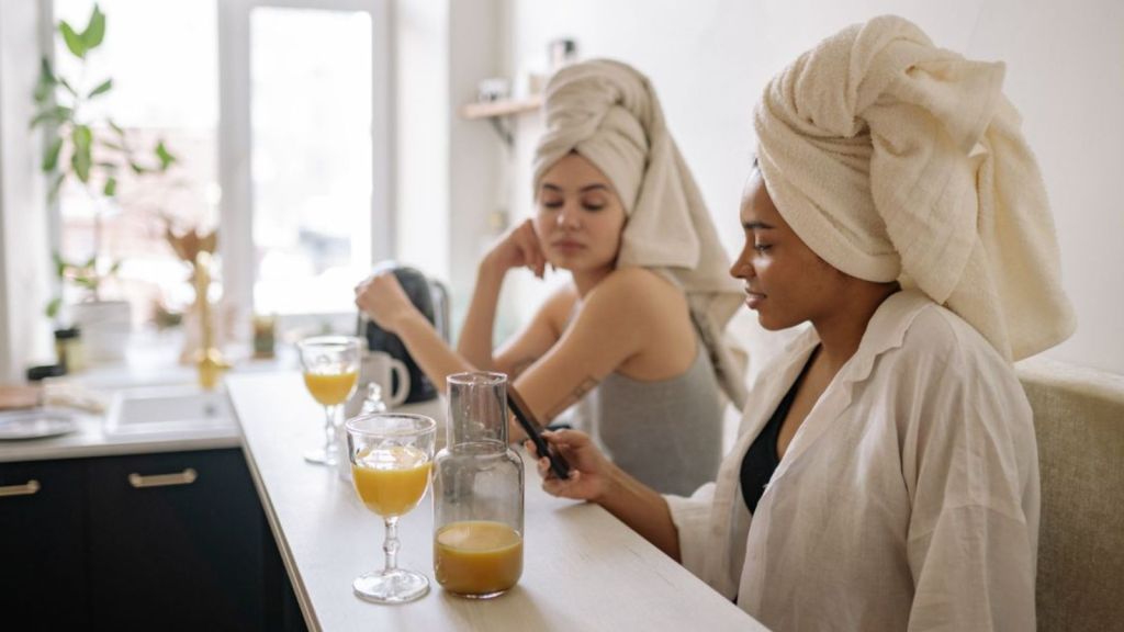 Two women with towels on their hair talking while drinking juice
