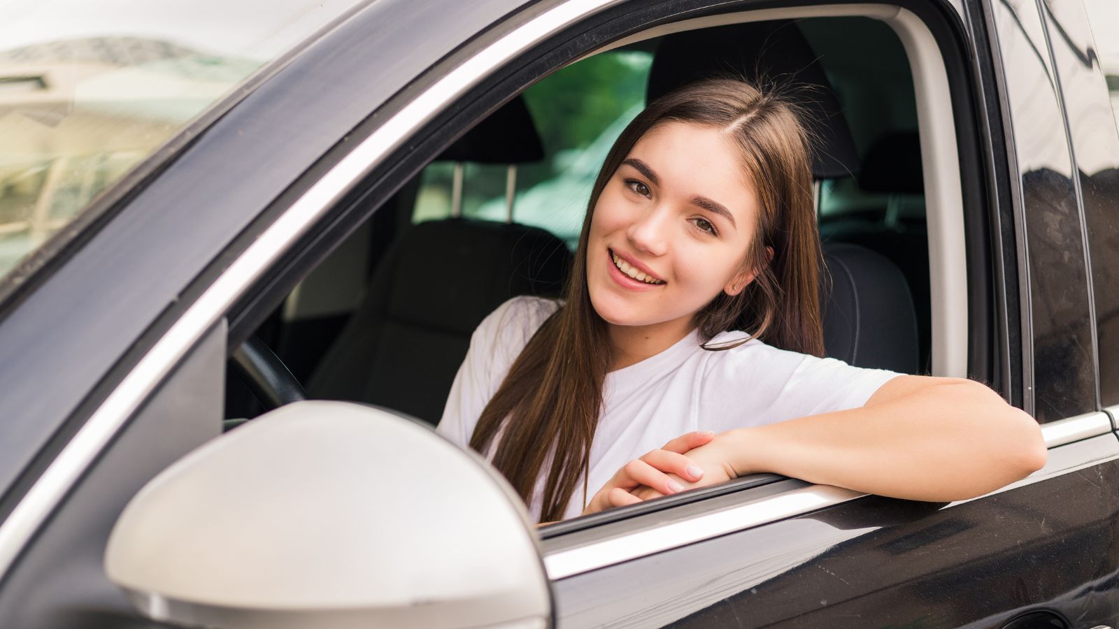 A Woman Sets Strict Rules For Her Stepdaughter’s Car Use, Sparking An Argument Over Safety And Independence Teenage girl smiling while looking out the window from the driver's seat of a car