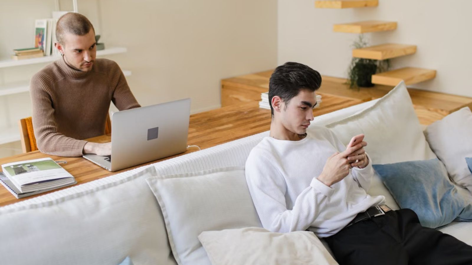 Two men hanging out in the apartment, busy with their personal stuff