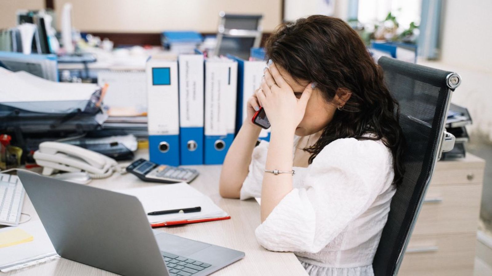 Woman talking on the phone and covering her face while in the office