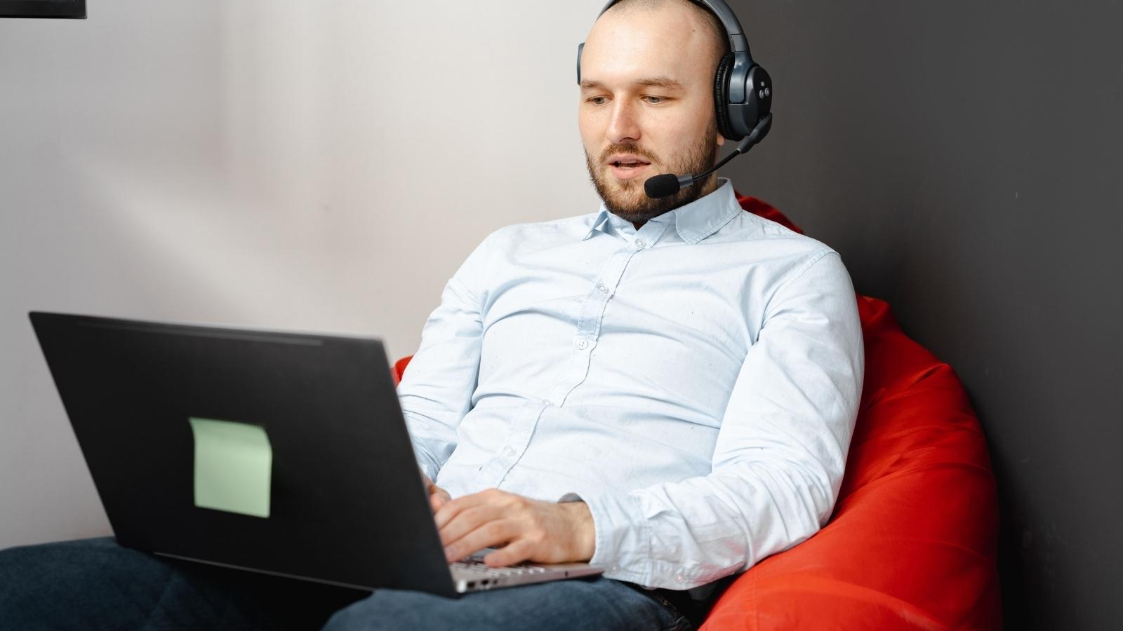 bald man using a headset typing on laptop