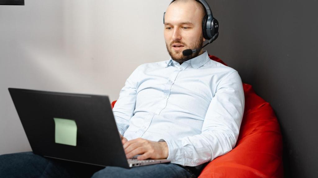 bald man using a headset typing on laptop