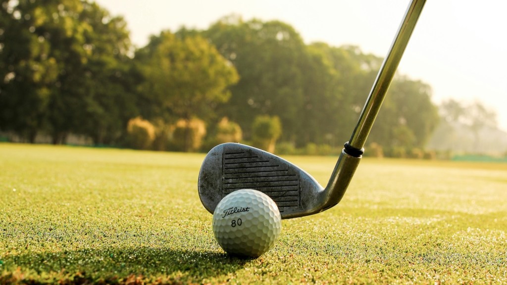 golf club about to hit a golf ball on the green