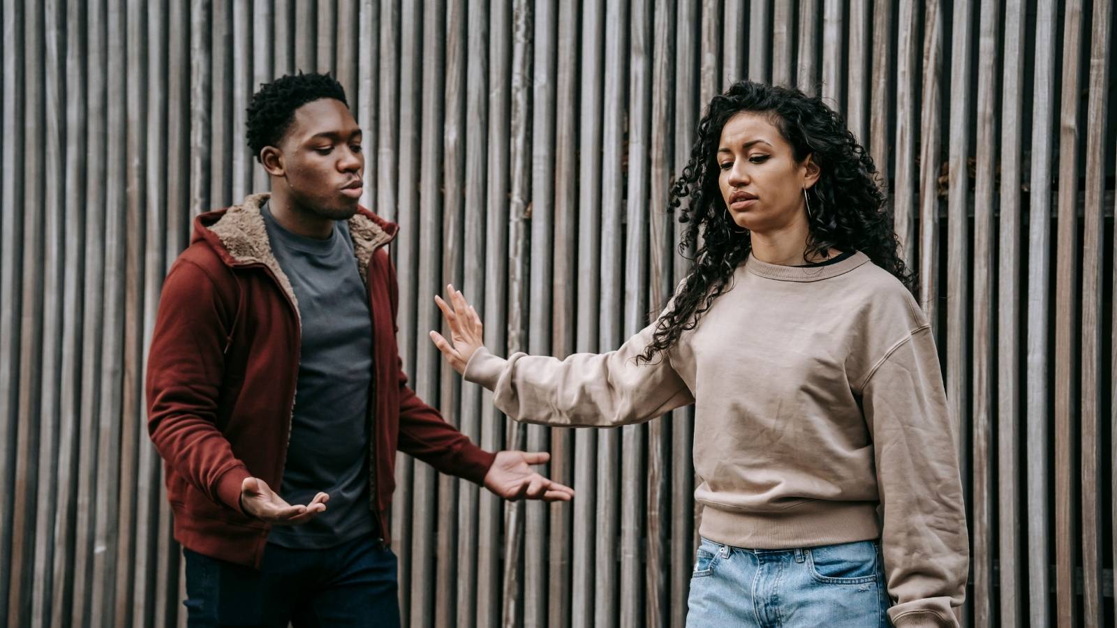 man and woman arguing in front of a wooden wall