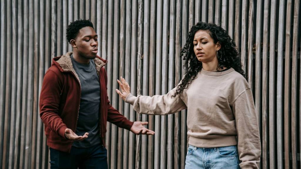 man and woman arguing in front of a wooden wall