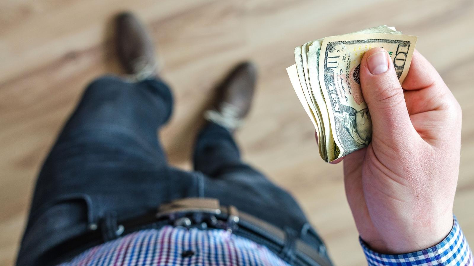 His Family Pressured Him Into a Cruise and Then Called Him Selfish for Not Wanting to Pay for It — Now Hes Thinking About Backing Out man holding a wad of cash