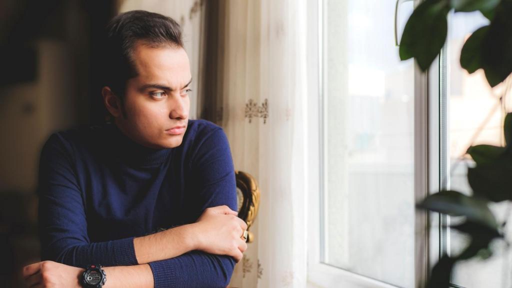 man in blue sweater looking out window