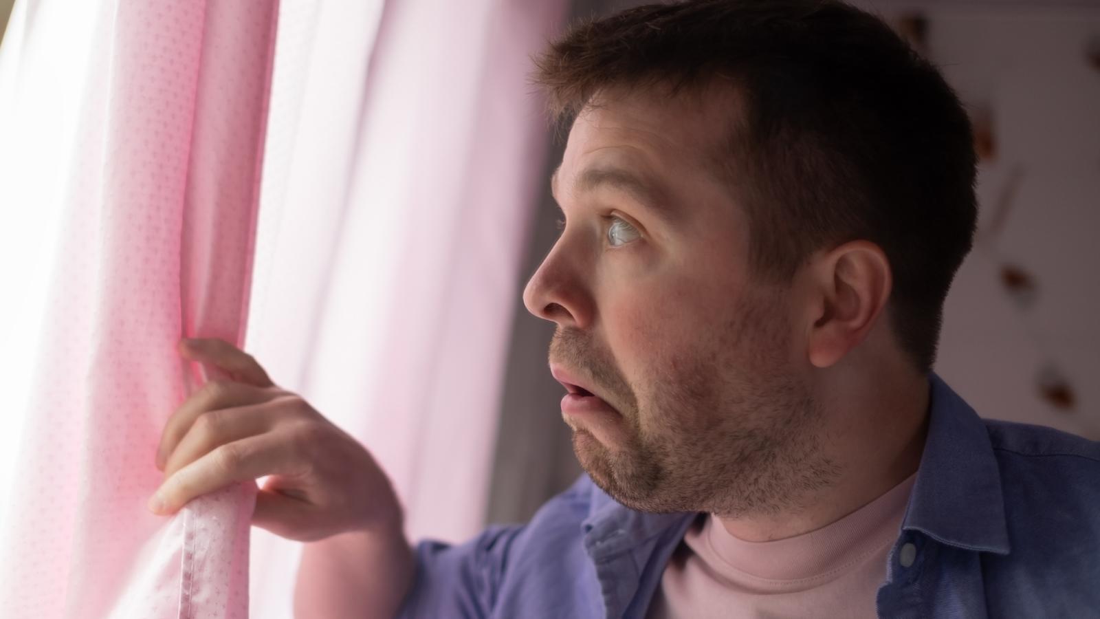 A Mans Neighbor Smokes Right Outside His House And Hes Tired Of It, But Hes Not Sure Whether To Confront Him man looking out a window