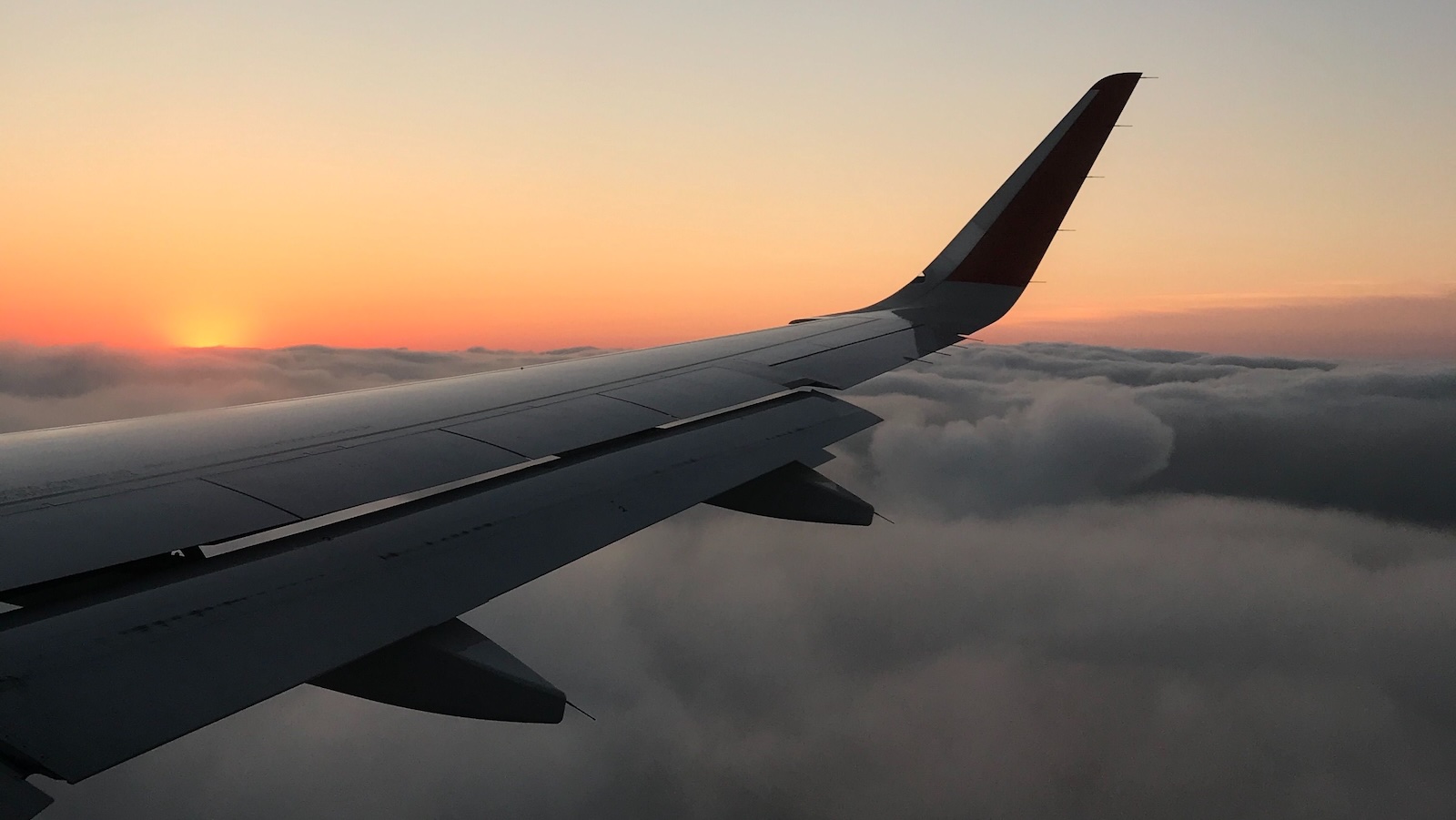 She Spent a Month in Europe Split Evenly Between Two Families — Her Best Friend Says That Makes Her Selfish plane traveling through clouds with sun setting behind it