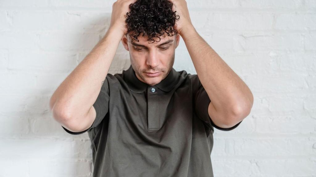 stressed curly haired man putting hands over head