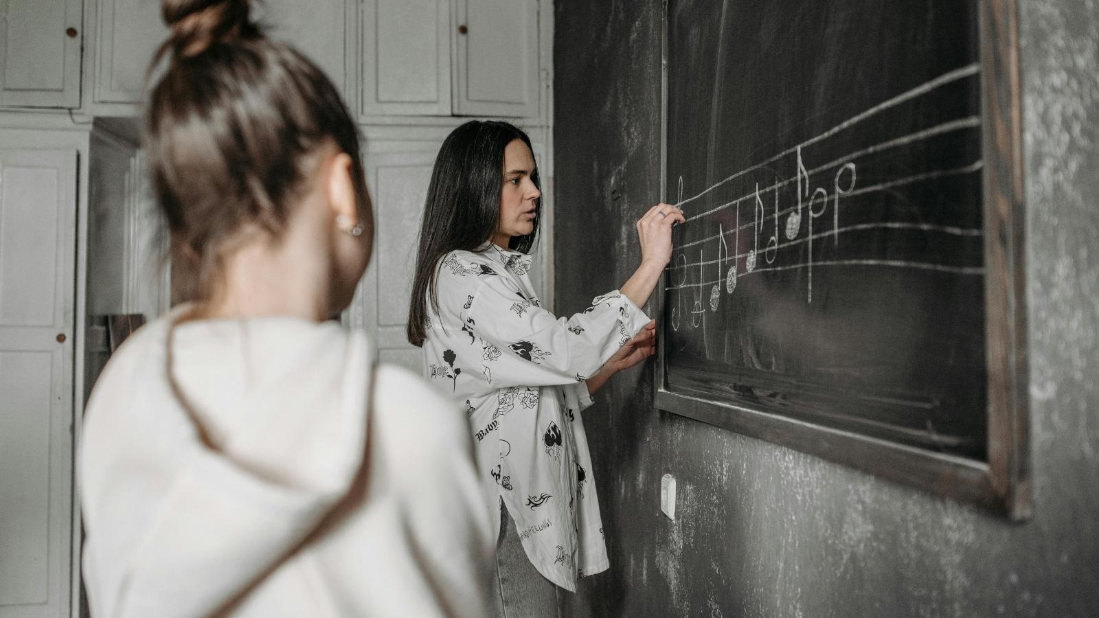student watching her music teacher draw on chalkboard