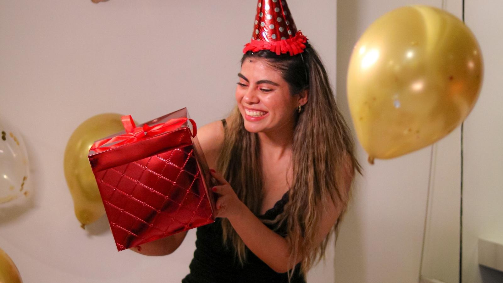 Woman Pushes for Luxury Birthday Gift, Then Gets Blasted by Friends for Secretly Charging Them Extra woman holding up a red birthday gift