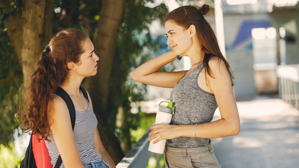 2 female students talking outdoors under a tree