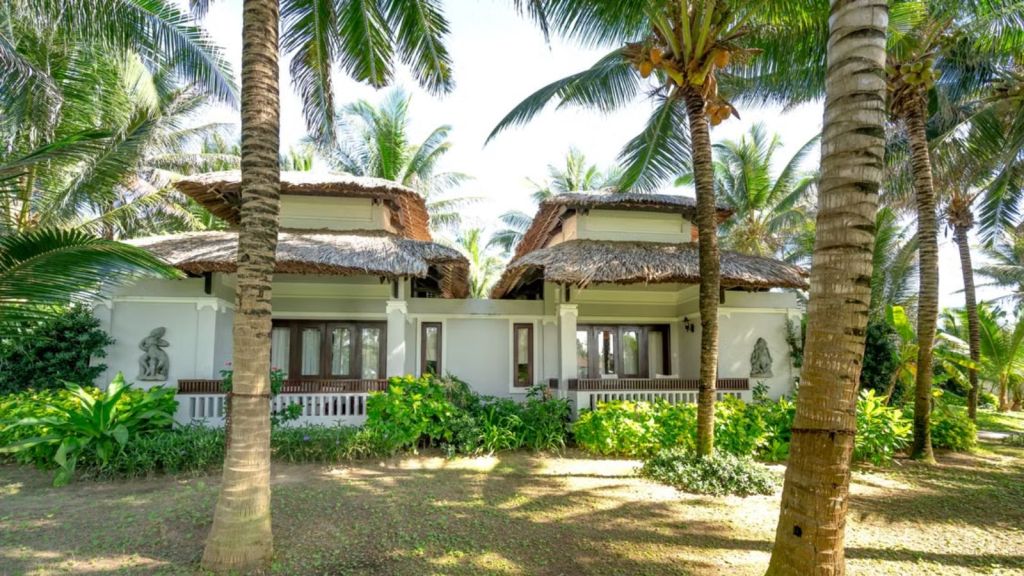 A tropical villa with coconut trees and lush plants on the surroundings
