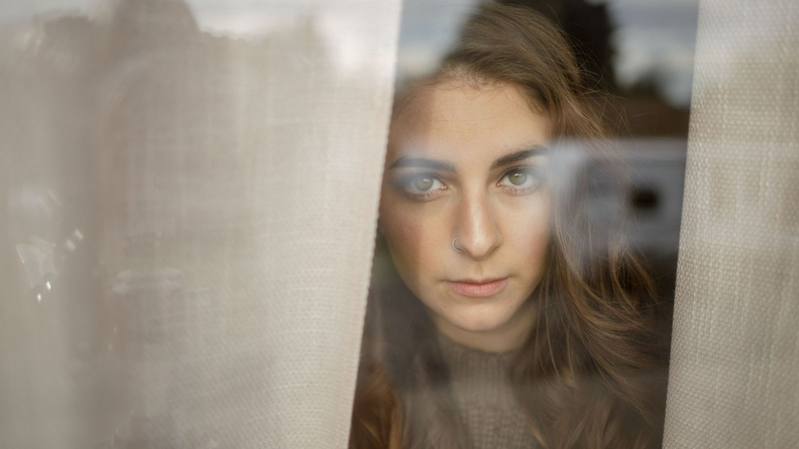She Thought Her Neighbor Just Had an Awkward Parking Spot. Then She Realized His Truck Was Positioned for a Terrifying Reason. A woman looking through curtains