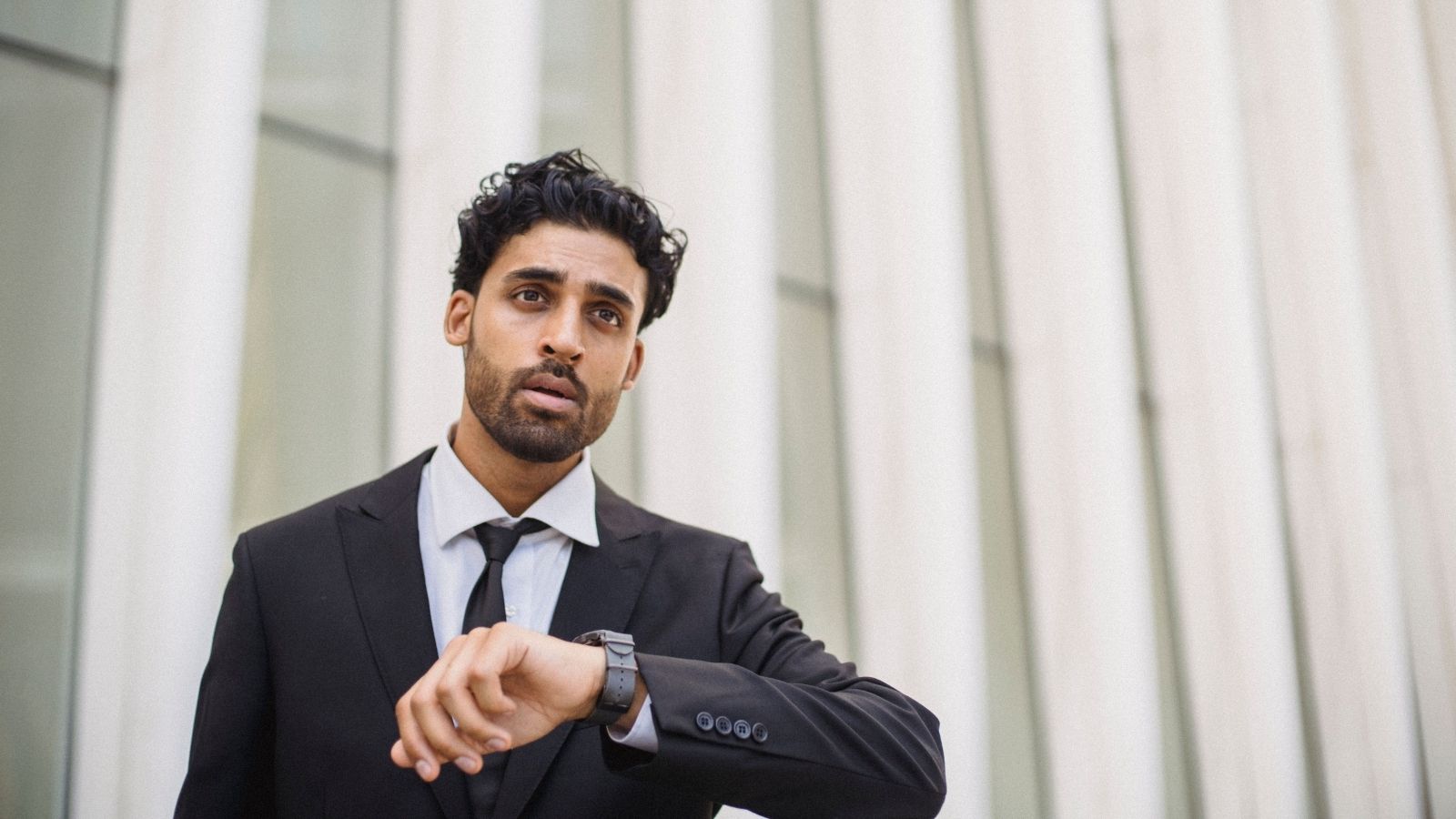 He Just Started a New Job and Is Desperate to Make a Good Impression, But His Girlfriend Keeps Making Him Late A man in a suit looking at his watch