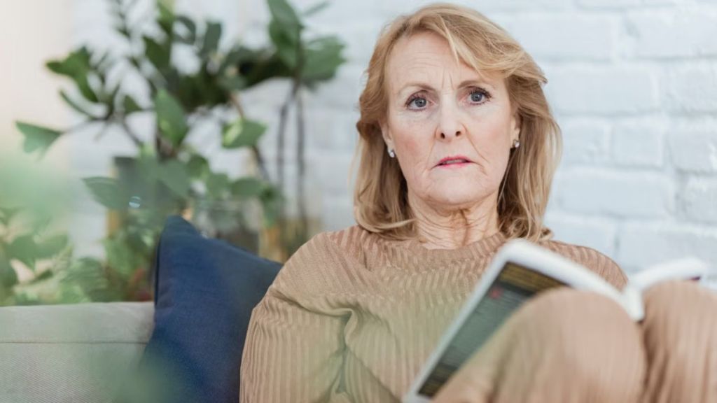 Old woman with a serious face sitting on the couch and holding a book