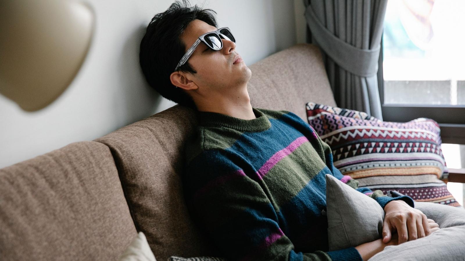 a Devoted Partner Is Reeling After His Girlfriend Tried to Demote Him for a Stranger Man being sad on the couch in sunglasses