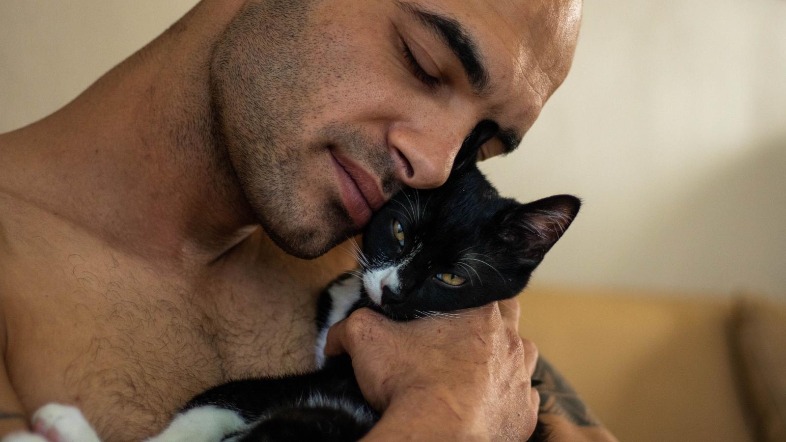 He Loves His Two Cats. Now His Girlfriend Is Accusing Him of Loving a Feline More Than Her—and He’s Speechless Man cuddling his black cat