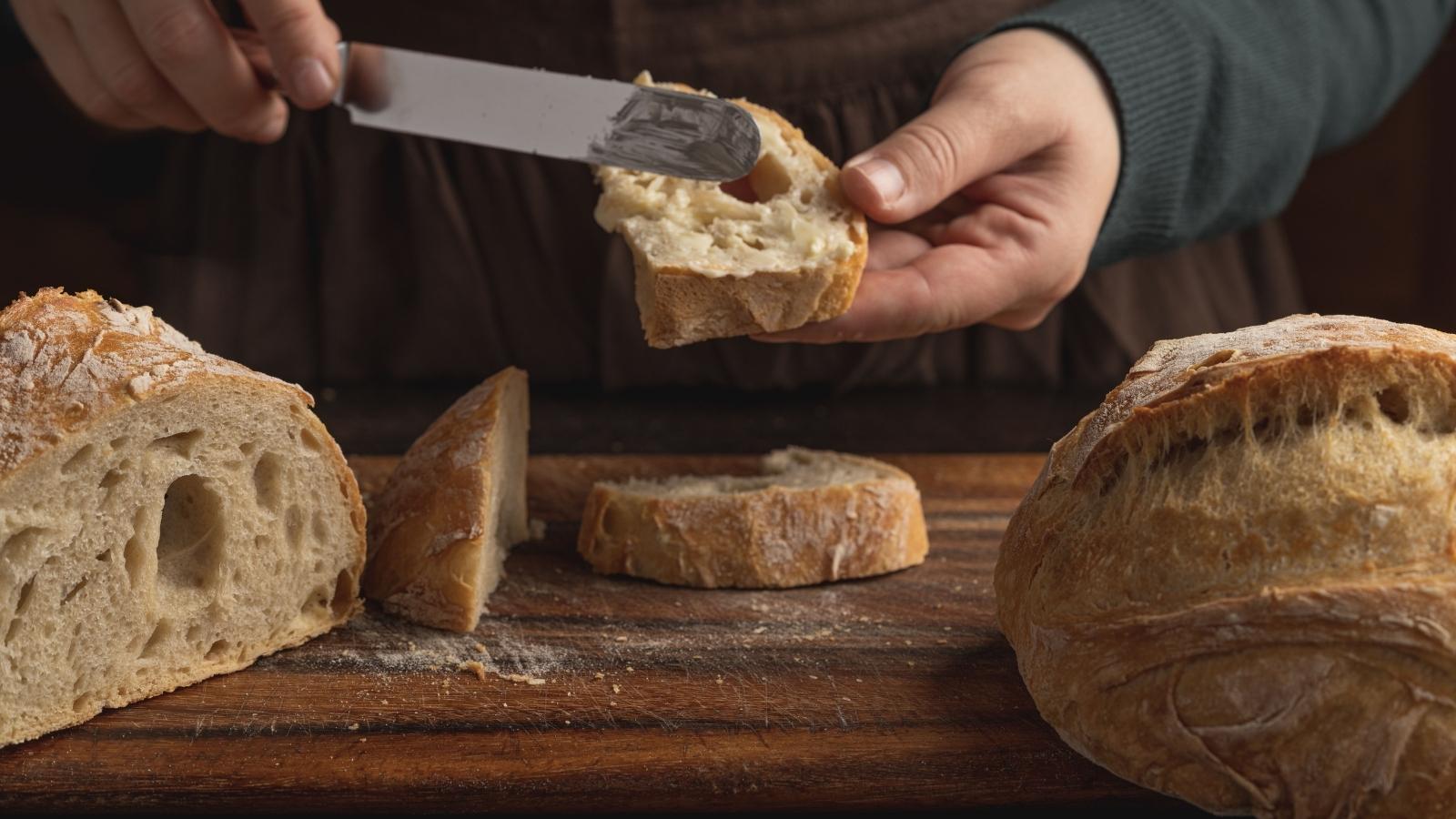 She Wanted to Share Extra Sourdough Starter for Free—Then Realized It Might Hurt Local Sellers Woman putting butter on sourdough bread