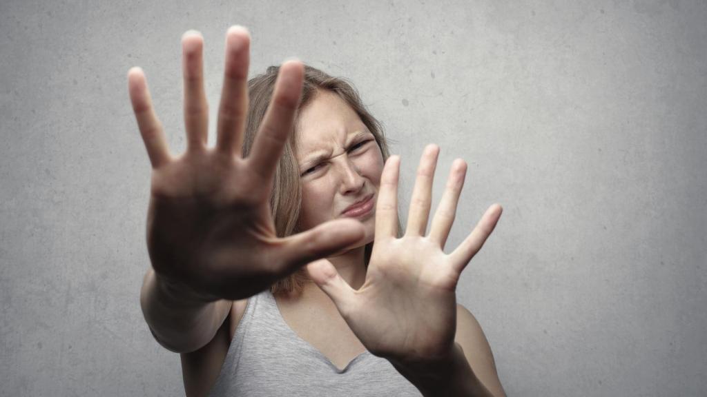 Portrait of a fearful woman in a gray tank top with hands pushed forward against a gray background.