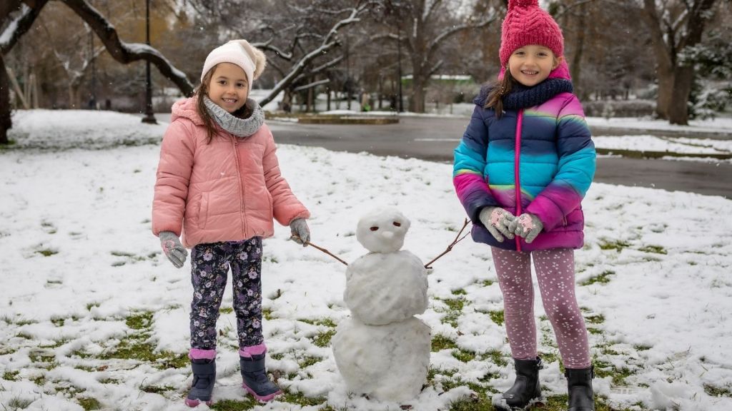 two little girls standing next to a small snowman