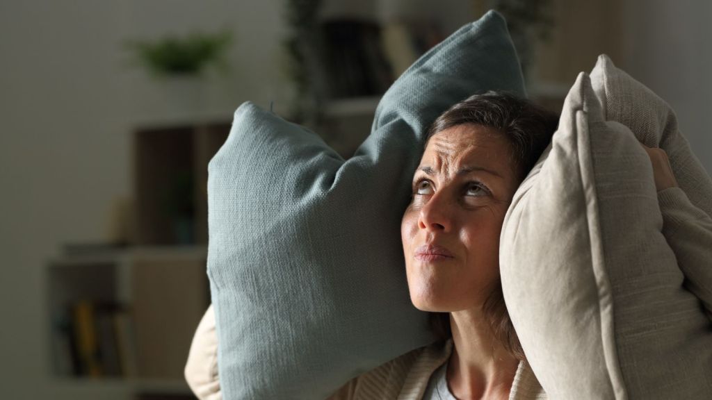 woman holding pillows over her ears and looking up