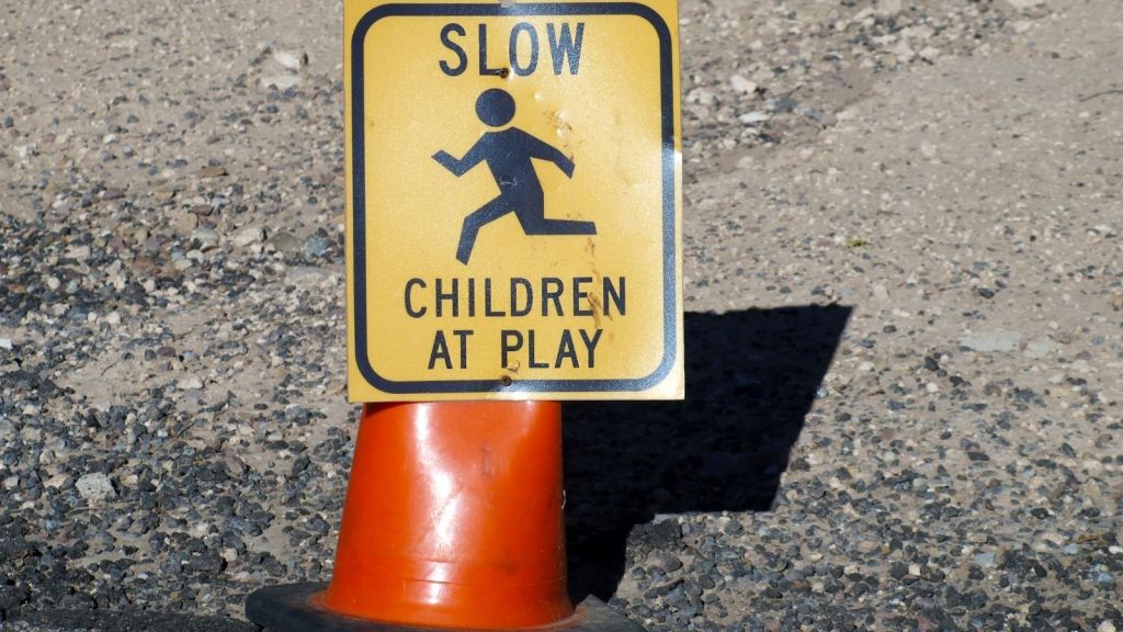 orange traffic cone with yellow sign attached that reads "slow children at play"