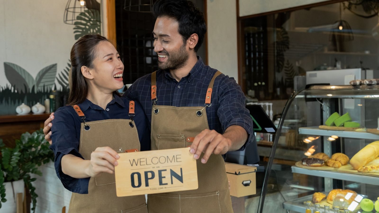 smiling couple holding sign that reads "welcome open"