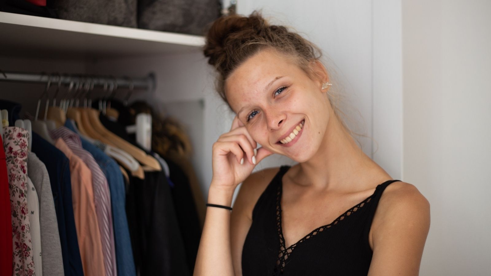 smiling teenage girl standing next to a closet full of clothes
