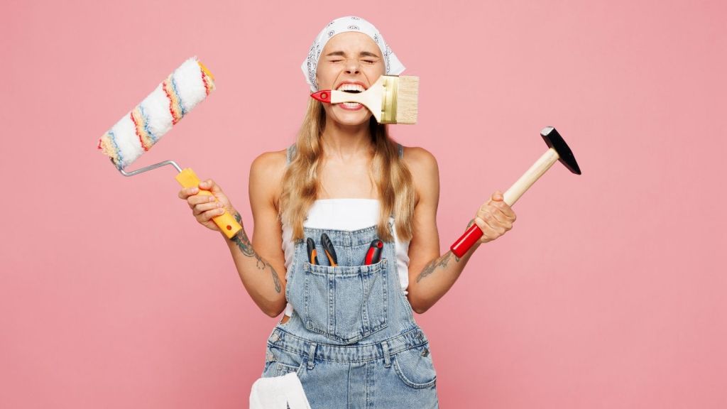 woman holding a hammer, paintbrush and paint roller