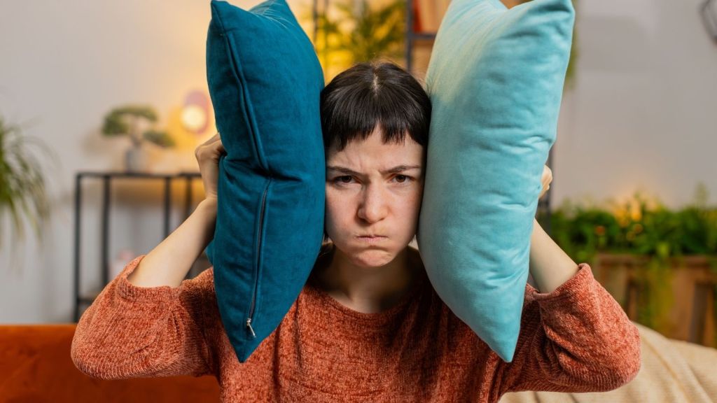 woman upset with noisy neighbors holding pillows to her ears