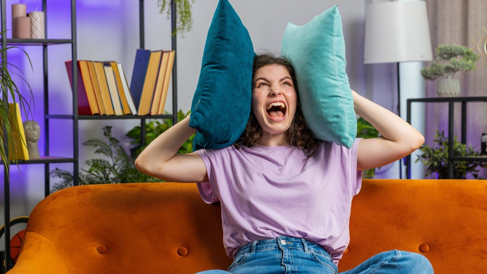 He Upgraded His Apartment Multiples Times to Find Peace—Only to Encounter Noisy Neighbors at Every Price Point woman yelling and holding pillows to her hears due to noise