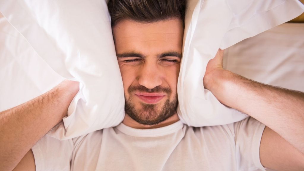 man trying to block out noise with a pillow