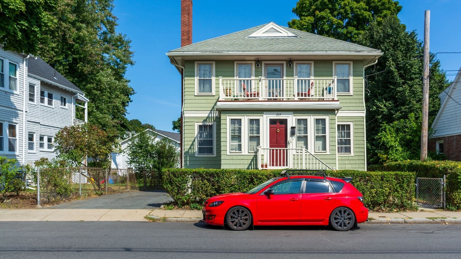 red car parked in front of green house