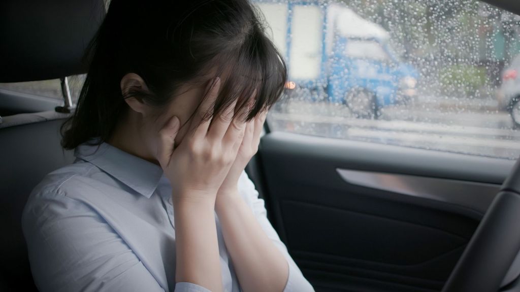 woman covering her face crying in the car