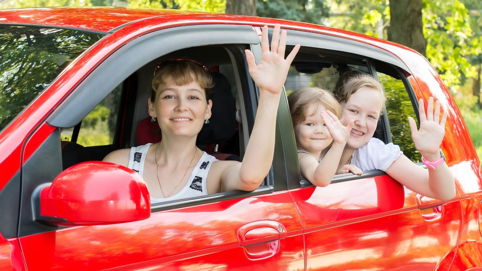 Her Husband Always Complains She Parks Too Far From the Store — While He Was at the ATM She Moved It to the Far Corner of the Lot mom and two kids waving from a red car