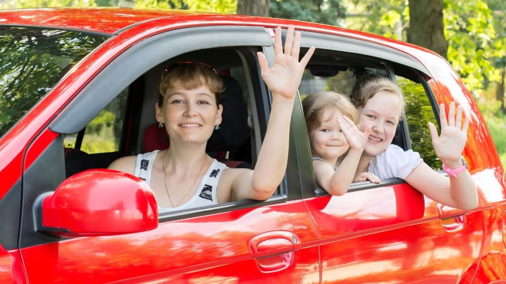mom and two kids waving from a red car