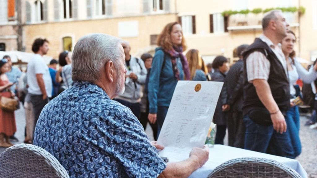 Old man looking at a restaurant menu while sitting at a table outdoors