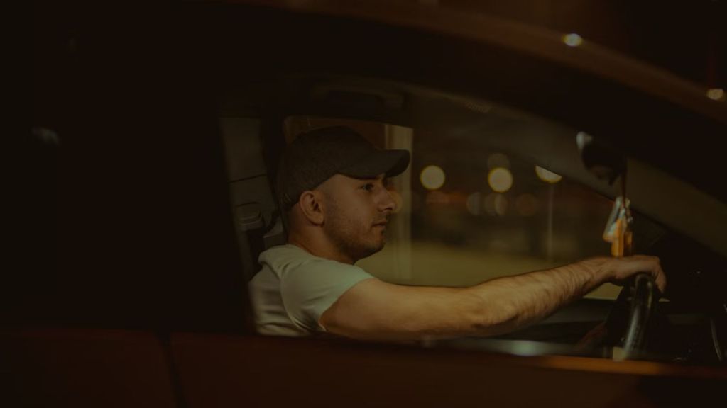 Man wearing a cap driving a car at night