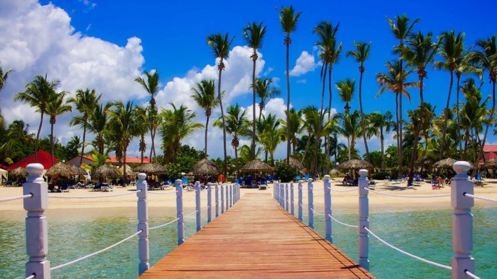 Wooden dock leading to a tropical beach resort with palm trees and clear blue waters in Dominican Republic