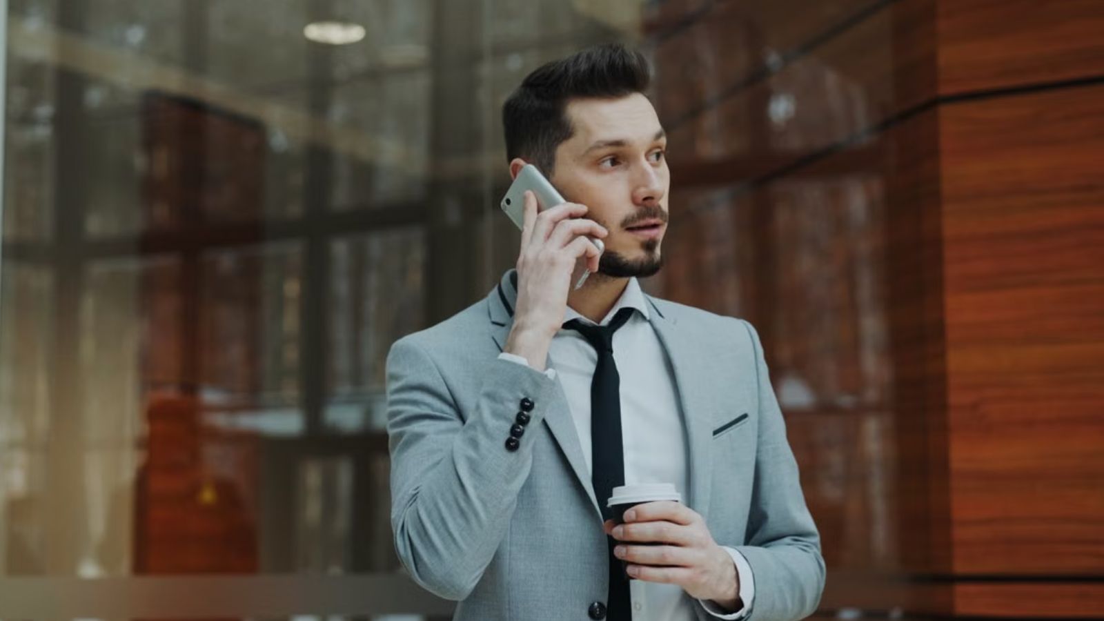 He Deleted Important Software and Ignored His Duties—But His Hotel Still Kept Him Around Man wearing suit is talking on his phone while holding a coffee cup