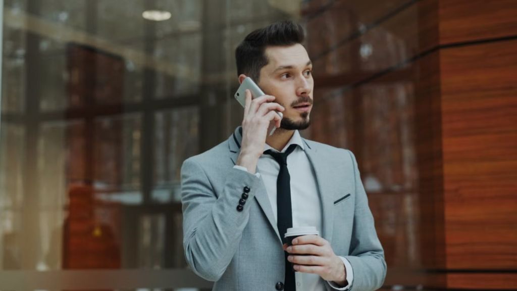Man wearing suit is talking on his phone while holding a coffee cup