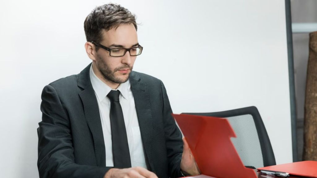 Employee in suit reading a document inside a red folder