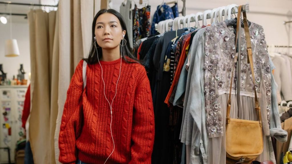 Asian woman wearing earphones and red sweatshirt in a clothes store