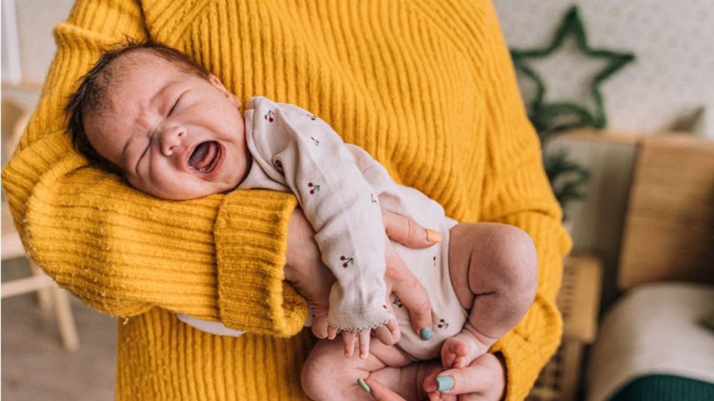 Woman in yellow sweatshirt carrying a crying baby